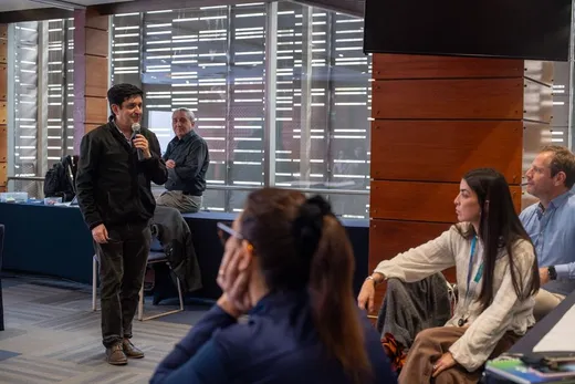 Una persona toma la palabra con un micrófono frente a un grupo que la escucha
