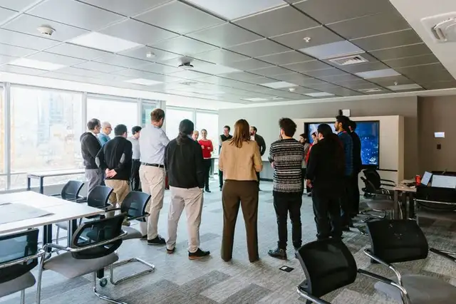 Un grupo de personas de pie, repartido por una sala luminosa durante un taller