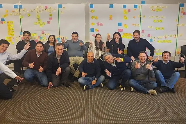 Un equipo sentado y de rodillas posando frente a paneles de notas adhesivas